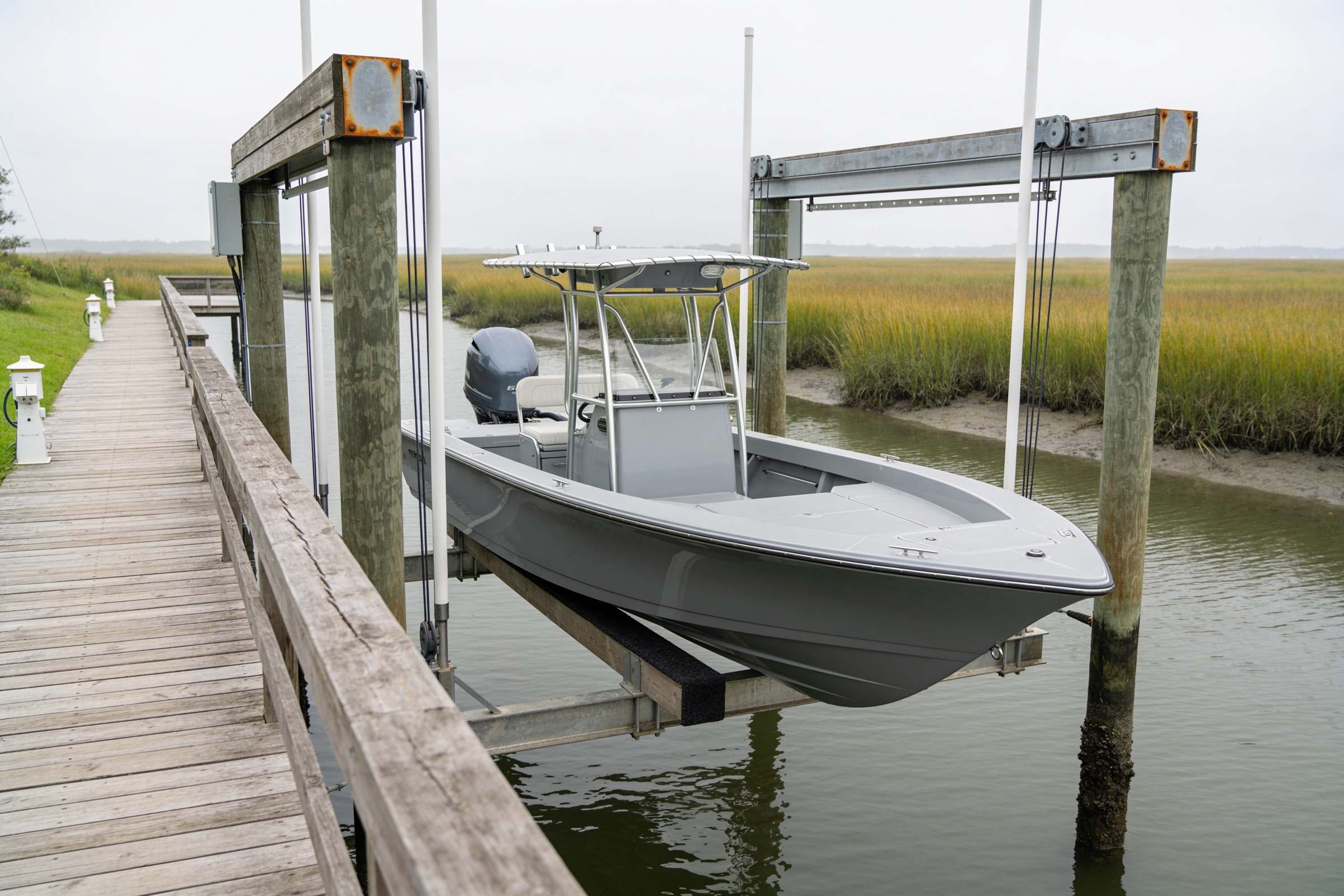 A finished private dock with a four-piling boat lift on a Hilton Head Island tidal creek at high tide, a center-console boat raised clear of the water on the lift, seen from the walkway.